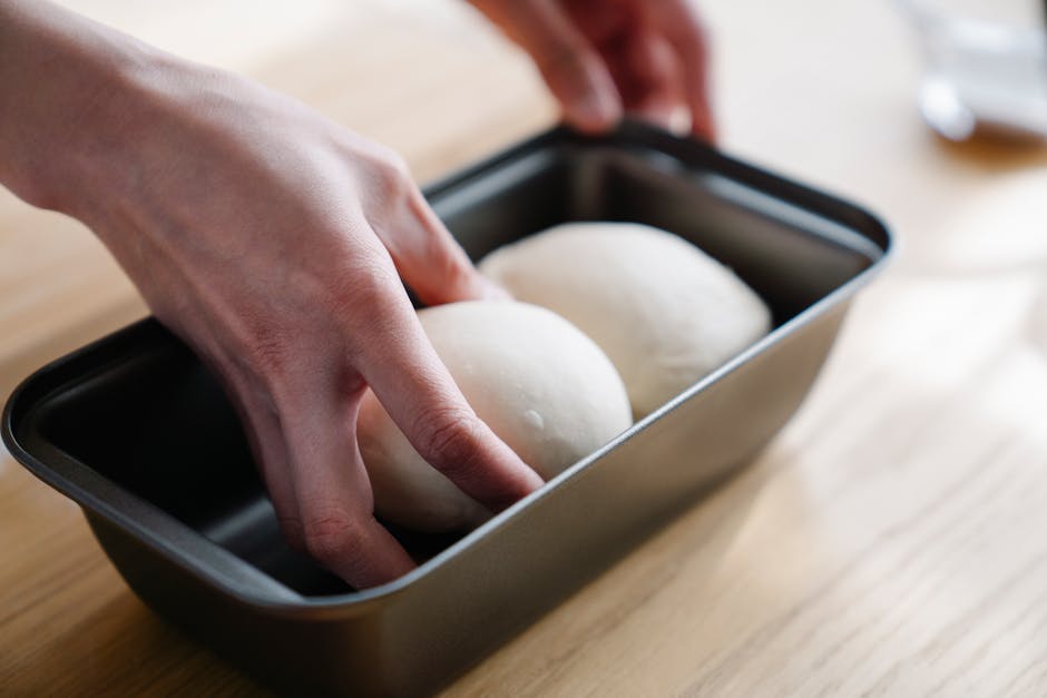 Close-up of hands placing dough balls in a tray, ready for baking.