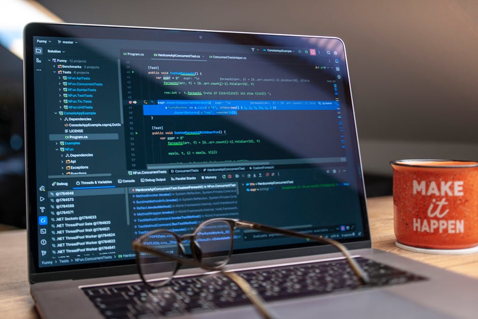 A laptop displaying code editor with a motivational mug that reads 'Make It Happen' on a workspace.