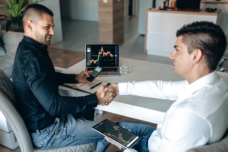 Two businessmen shake hands over a successful stock trading agreement using technology in a modern office.