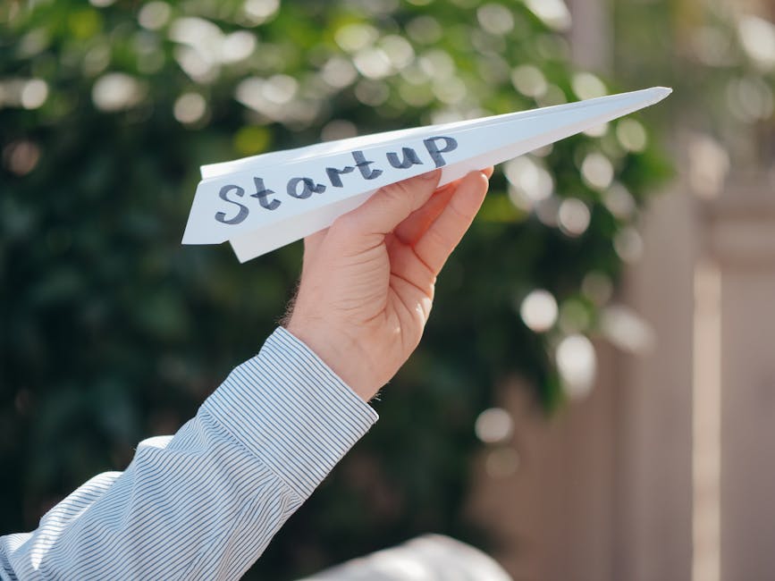 Close-up of a hand holding a paper plane with 'Startup' written, symbolizing a business launch.