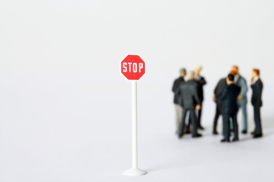 A miniature stop sign stands out with blurred figures in business attire, representing a conceptual business metaphor.