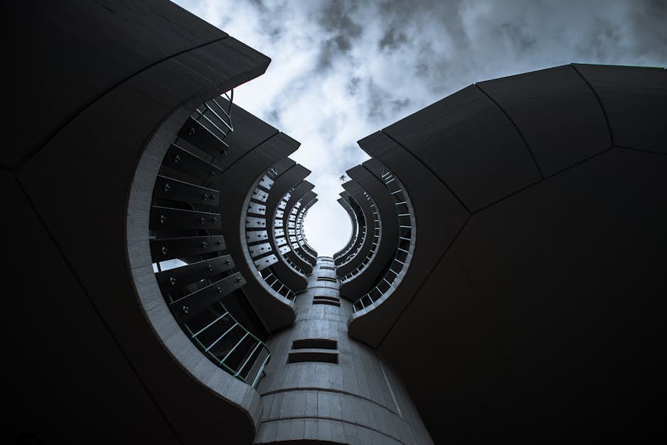 Dramatic low angle view of a modern circular tower against a cloudy sky, showcasing architectural design.
