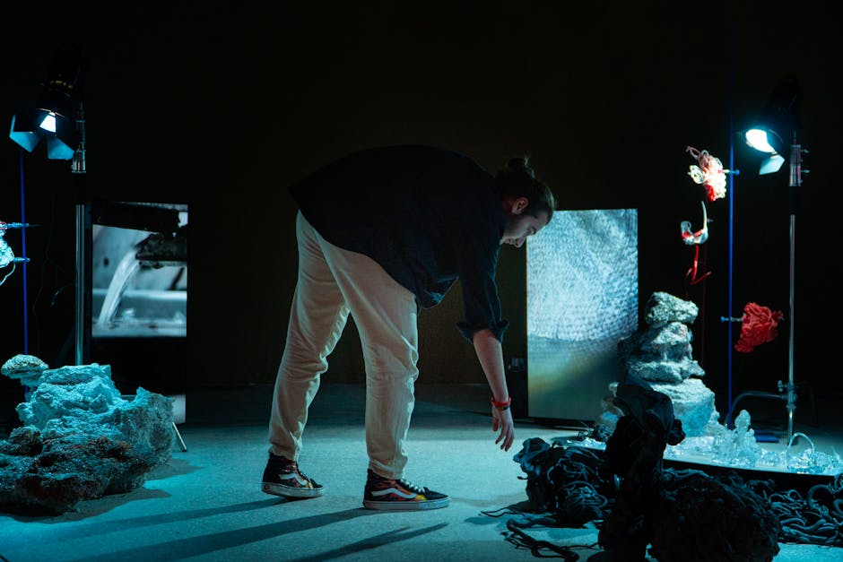 A man interacting with an artistic installation under dim lighting, featuring rocks and digital screens.