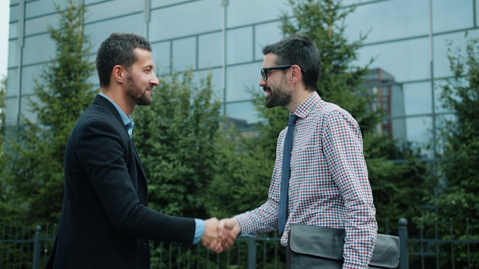 Two men shaking hands outside a modern office building, symbolizing business partnership.