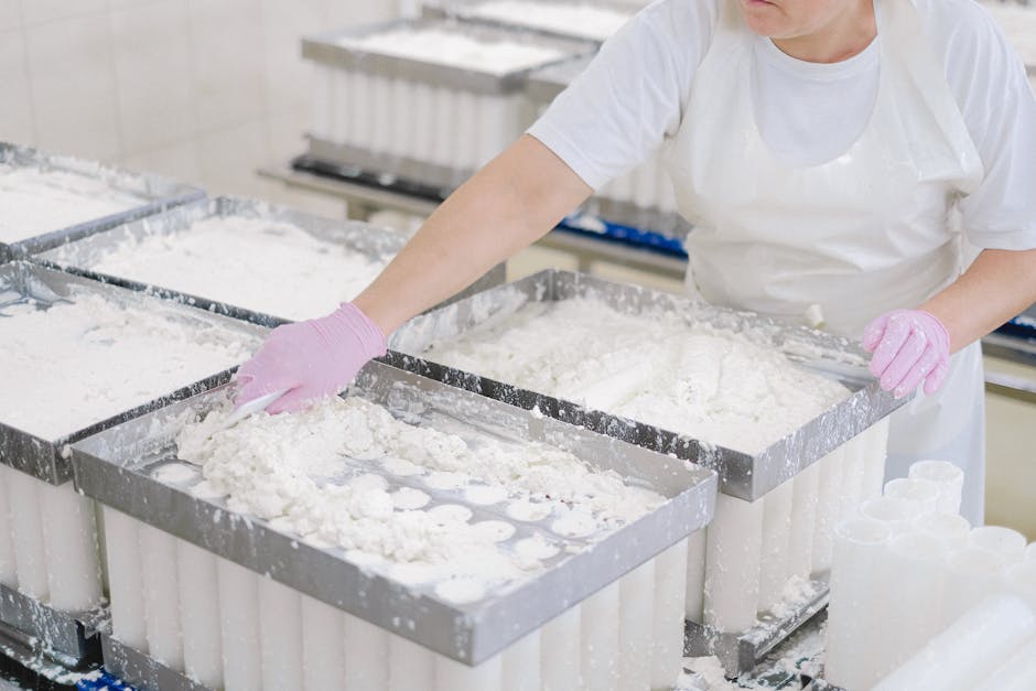 Worker in protective gear handling cheese curds in an industrial dairy setting.