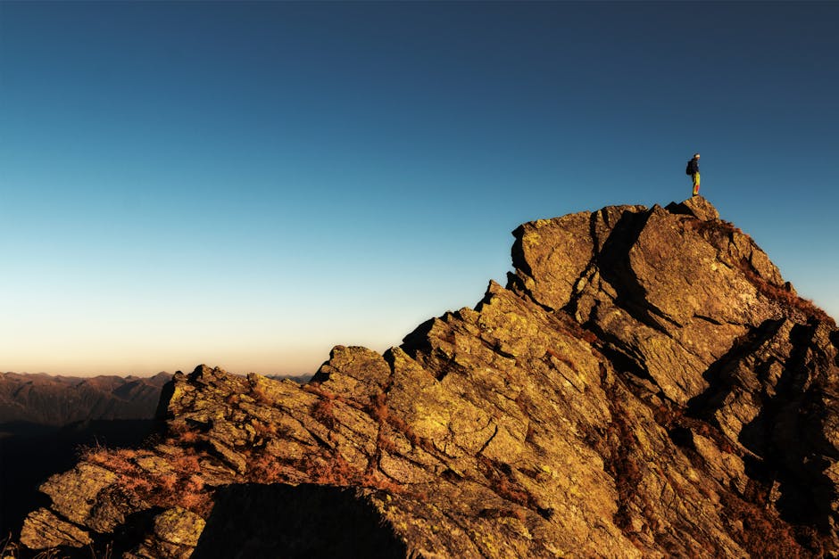 A lone hiker stands triumphantly atop a rocky mountain peak at sunrise, embracing nature and the view.