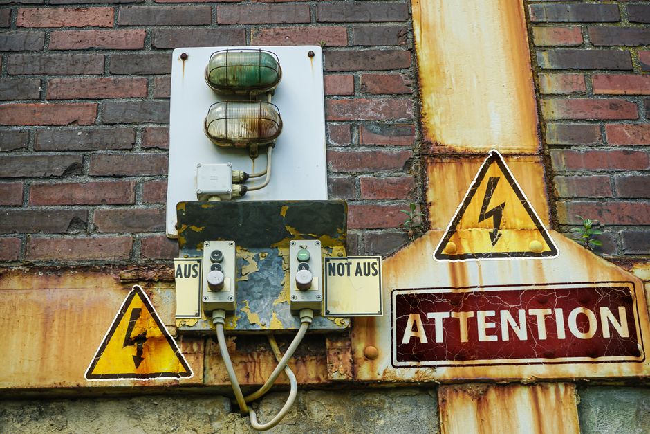 A close-up of an old, rusty warning sign and electrical components on a brick wall conveying caution.
