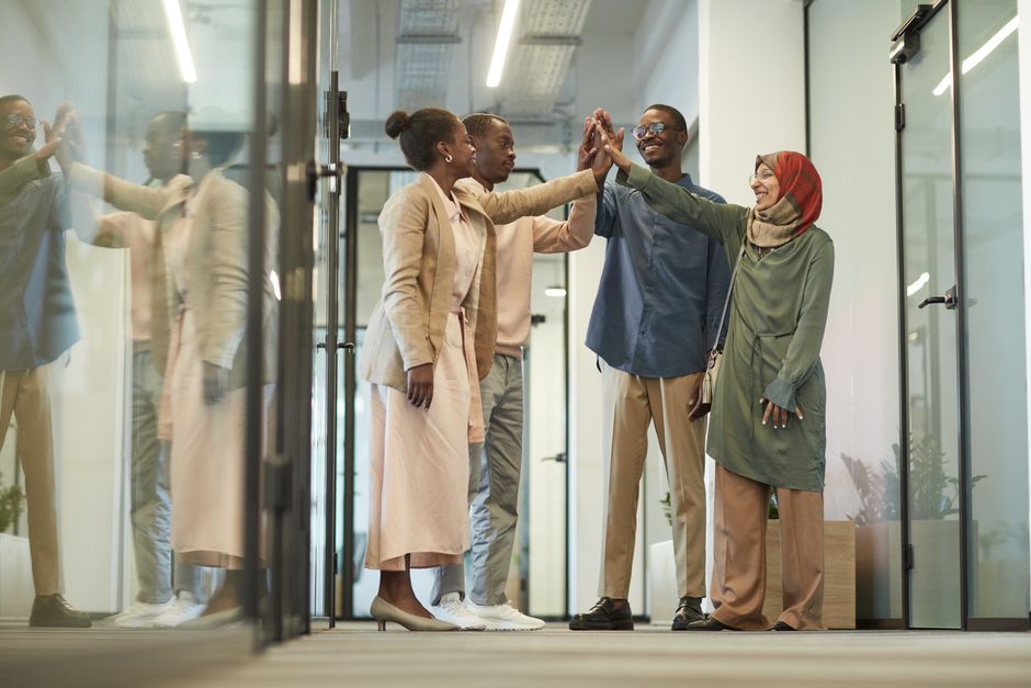 A diverse group of professionals celebrating with a high five in a modern office setting.